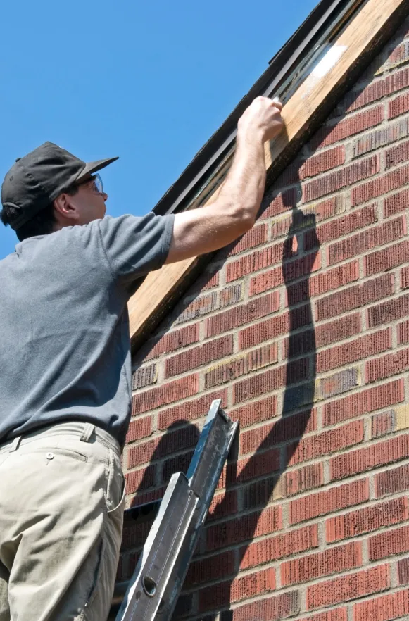 Professional painter on a ladder applying a fresh coat of paint to the trim of a brick house, ensuring a polished and updated look.