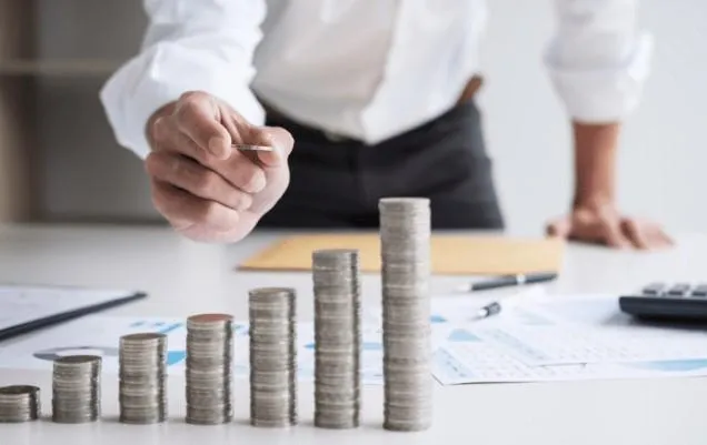Coins stacked up to a hand holing a lightbulb and other hand with pen on pad. Smart Thinking picture