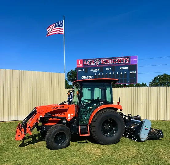 Bad Boy tractor on the LCA Knights baseball field with scoreboard and American flag in the background.