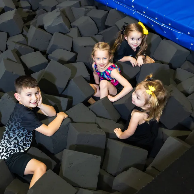 Children playing in a foam pit at a gymnastics center, promoting fun and teamwork in a safe environment.