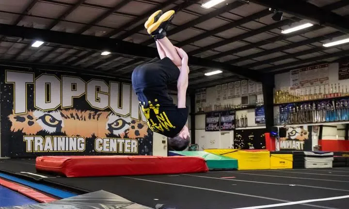 Athlete performing a backflip on a tumbling mat at Top Gun Training Center, showcasing skill and technique in a structured training environment.