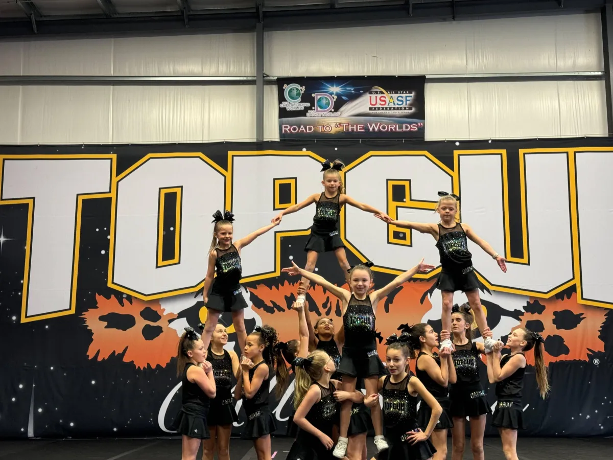 Cheerleaders performing stunts and routines in front of a "TOP GUN" backdrop, showcasing teamwork and athleticism in a recreational cheerleading program.