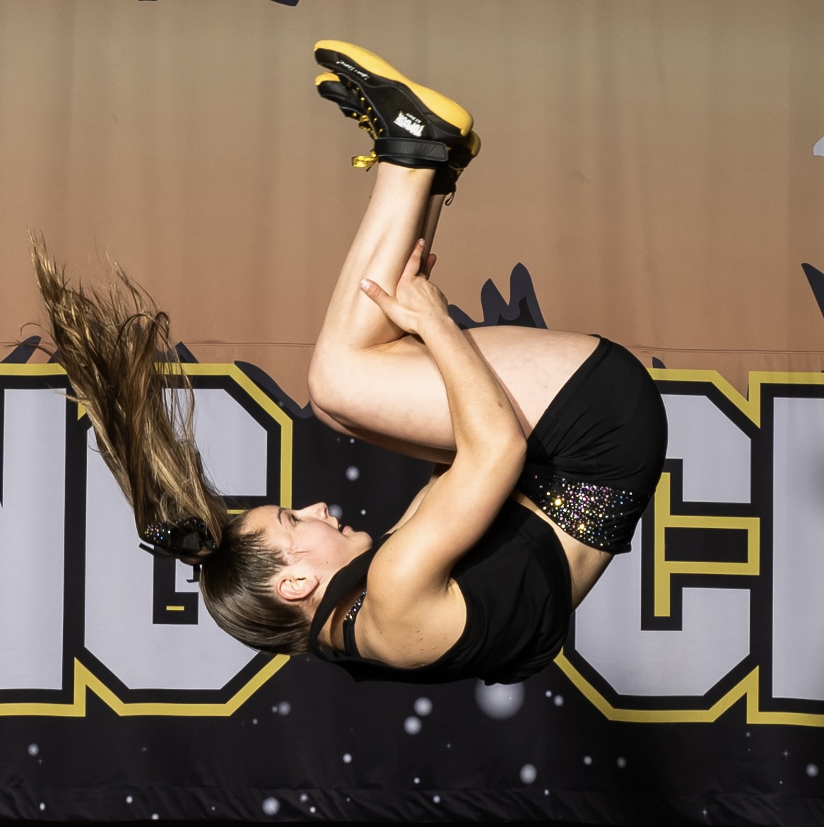 Girl performing a high-flying acrobatic move in a competitive cheerleading event at Top Gun Ohio, showcasing athleticism and skill in a vibrant environment.