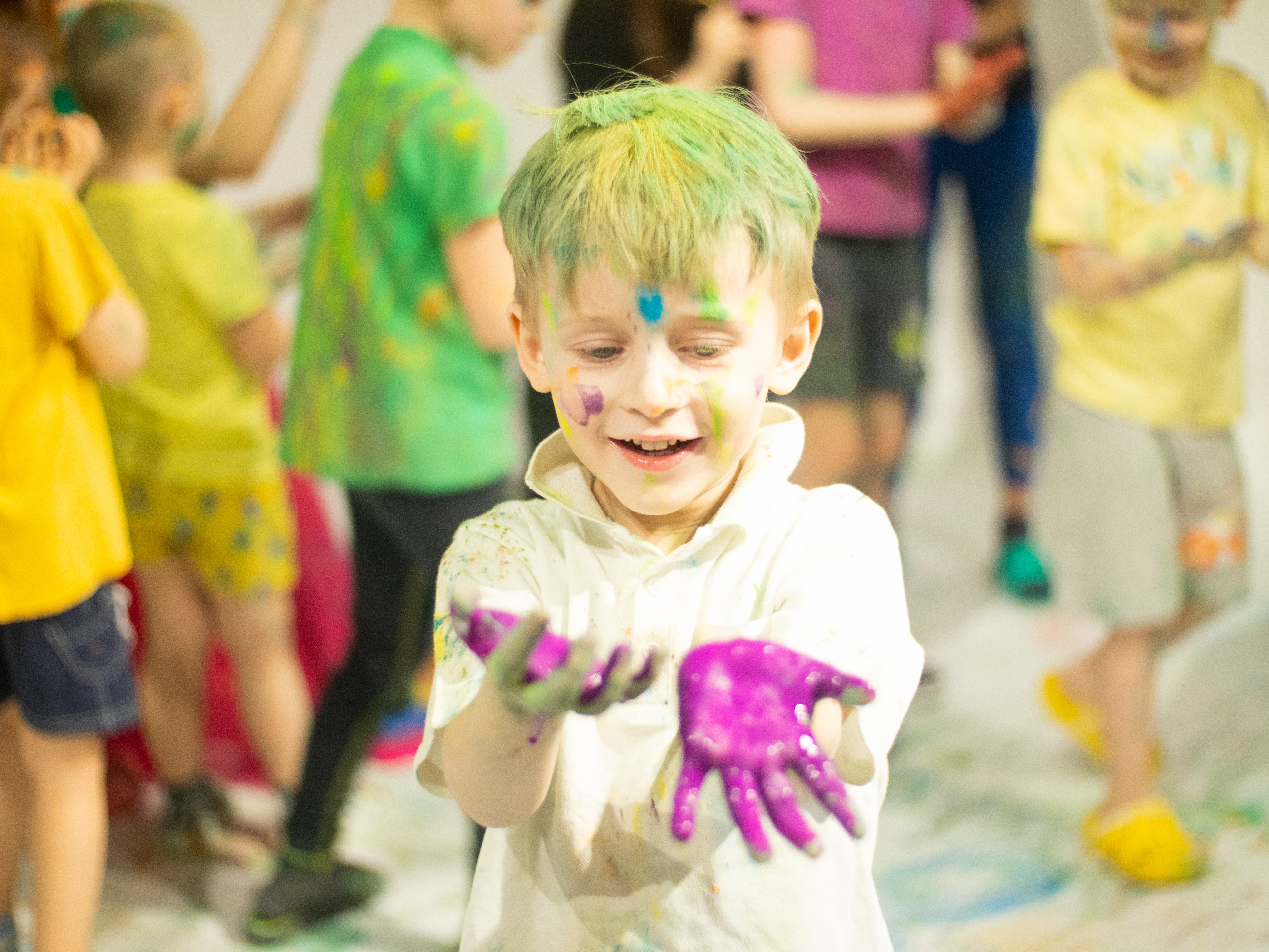 Child with colorful hands, smiling and enjoying a creative activity, surrounded by other children in a playful, vibrant setting, representing fun and engagement in recreational camps at Top Gun Training Center.