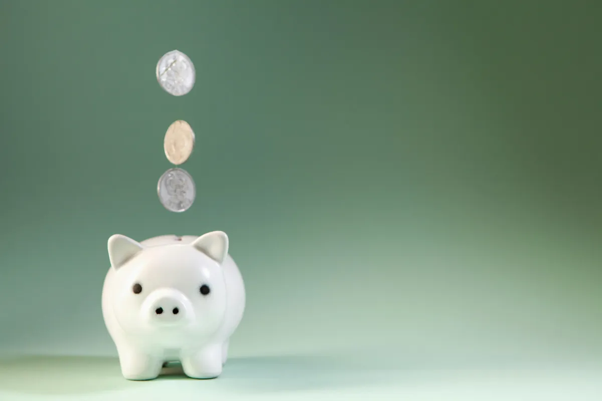 Small white piggy bank with coins falling into it