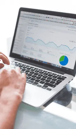 Person arbeitet an einem Laptop mit geöffnetem Google-Analytics-Dashboard, das Besucherstatistiken und ein Kreisdiagramm zeigt.