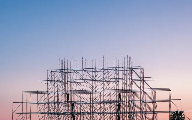 Silhouettes of workers on scaffolding against a pink and blue dusk sky, representing the structural work that makes composable architecture hold together