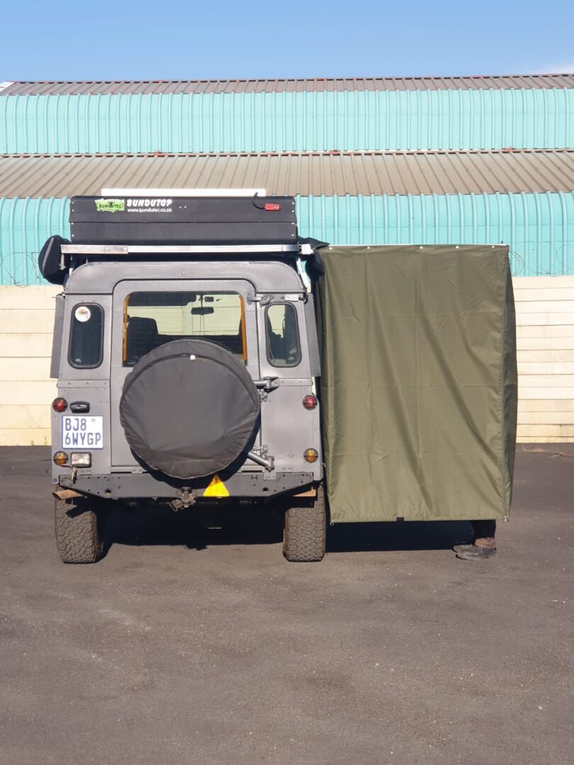 A Land Rover with a rooftop tent and a green side awning extended.