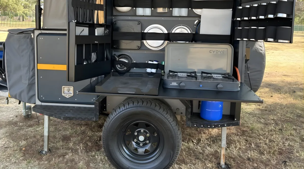 Outdoor kitchen setup on a camping trailer with stove and organized storage.