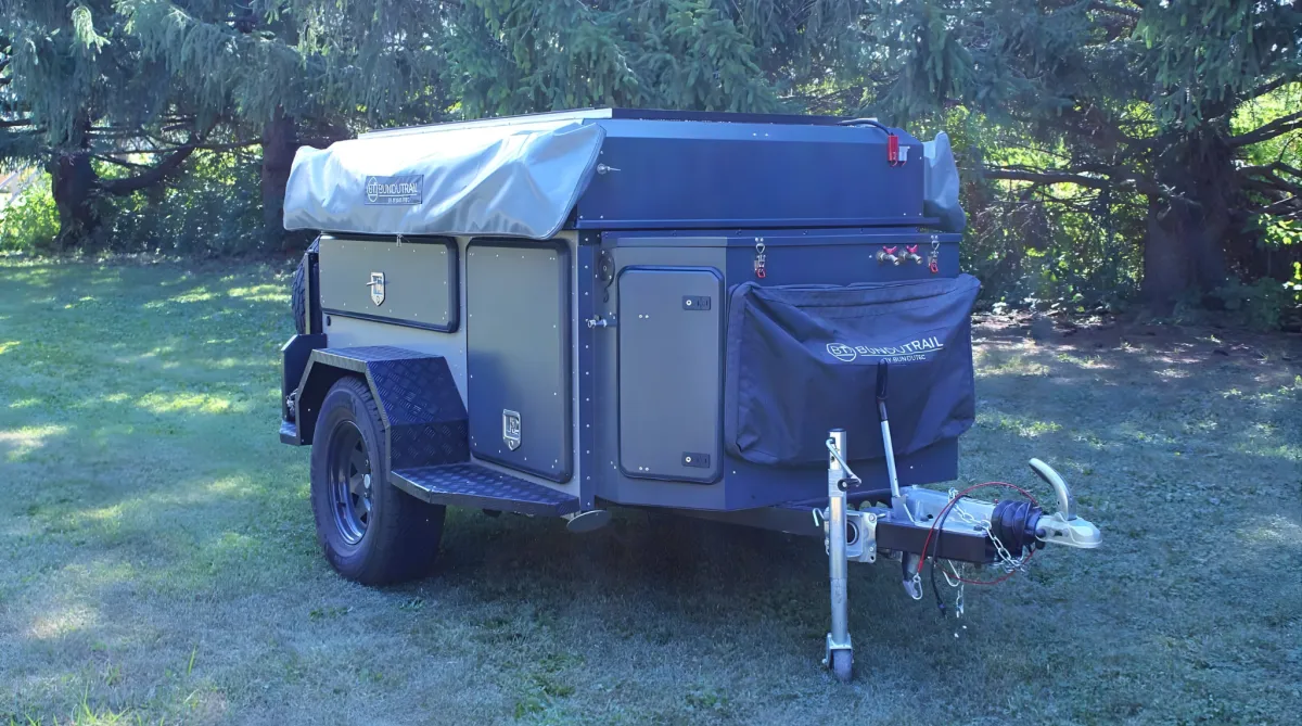 Off-road camping trailer with gear compartments parked on grass.