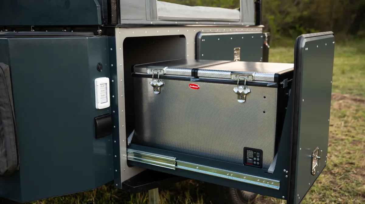 Camping trailer with a large awning set up beside a pond.