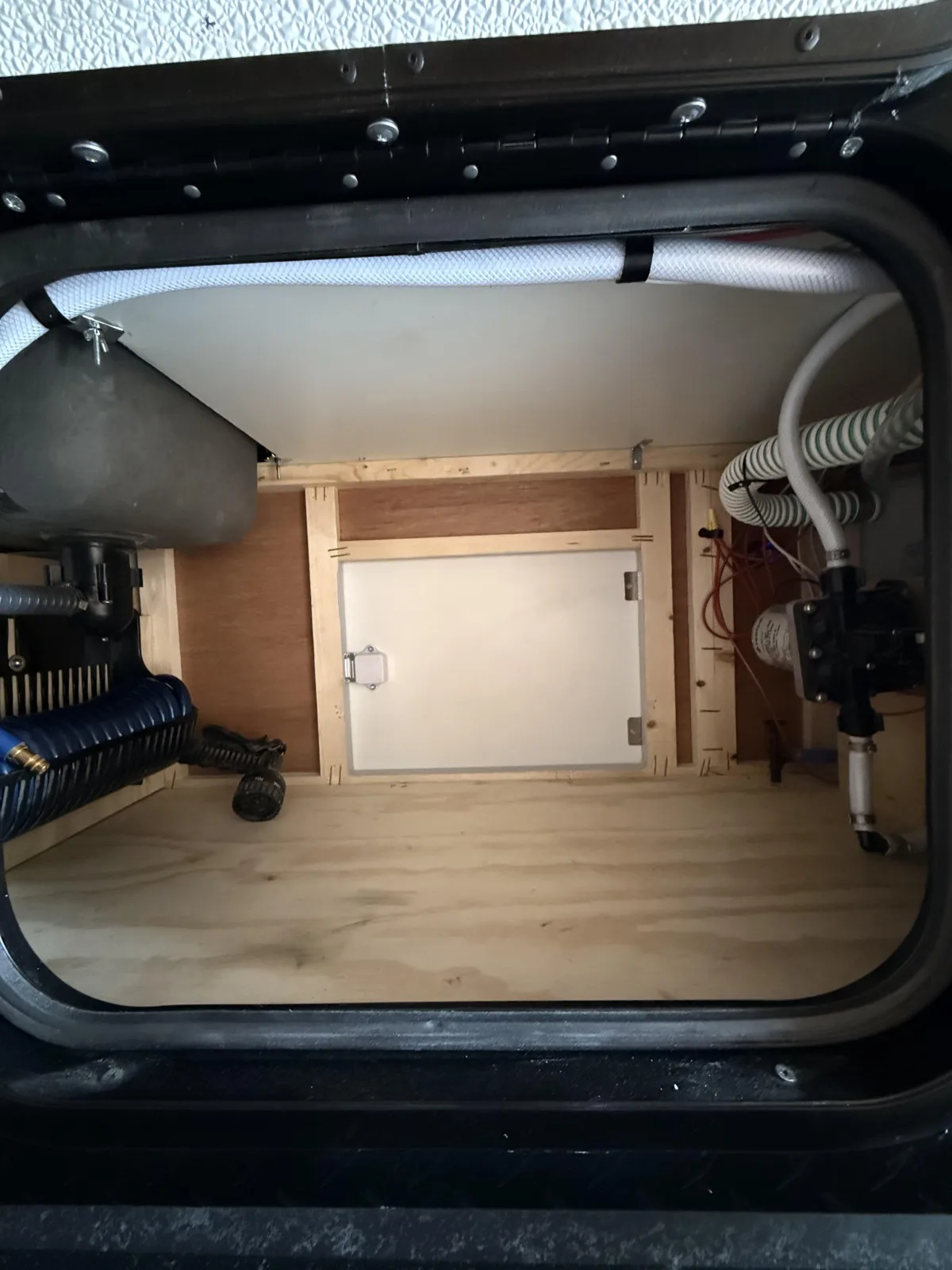 Riptide camper front storage compartment showing water pump, hoses, and interior access panel
