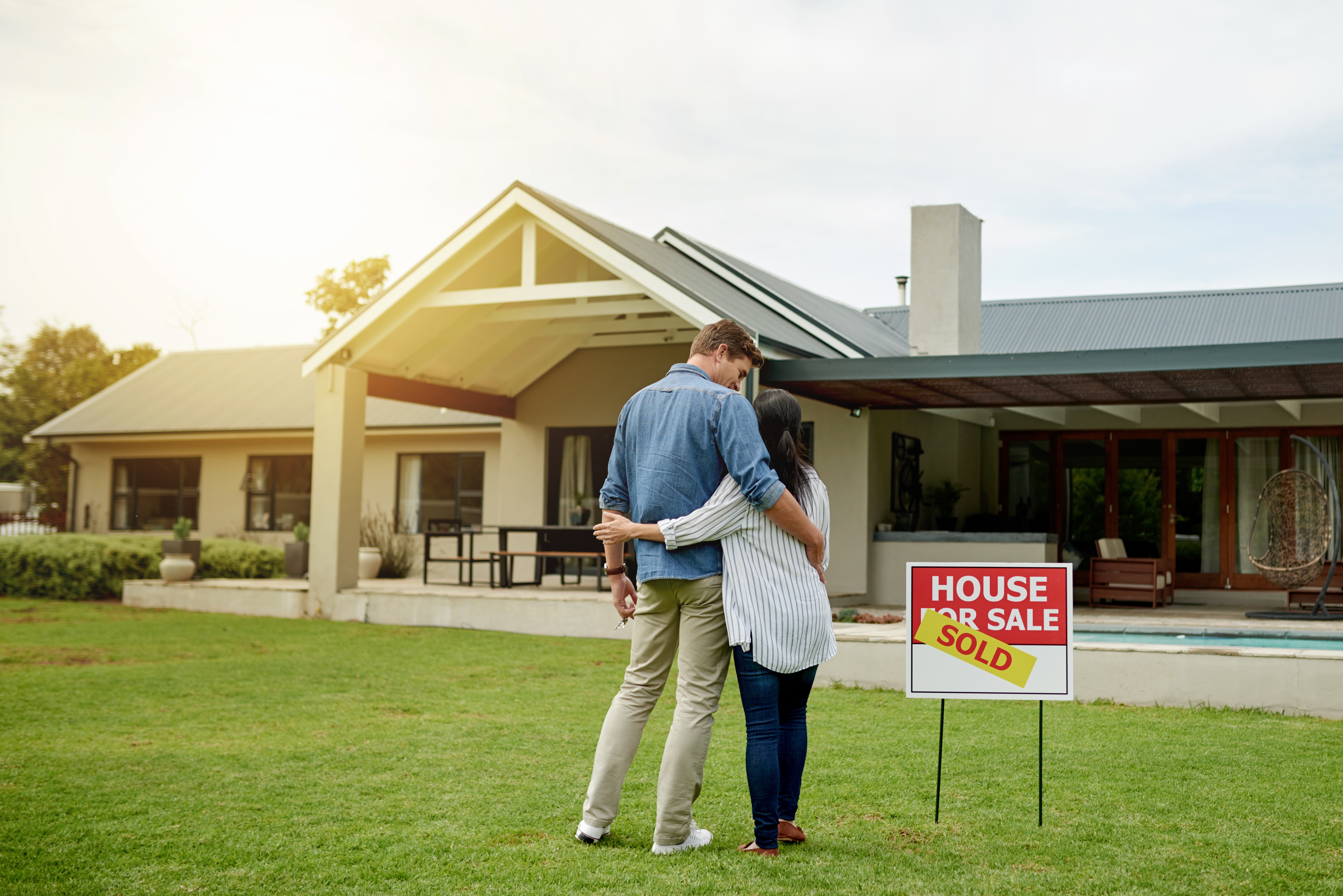 couple hugging in front of house with sold sign 