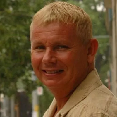 A portrait photo of Stephen Clarke, smiling warmly and looking at the camera. The background features a softly blurred outdoor scene with greenery, suggesting a friendly and relaxed atmosphere. This image accompanies a testimonial, emphasizing trust, approachability, and satisfaction.