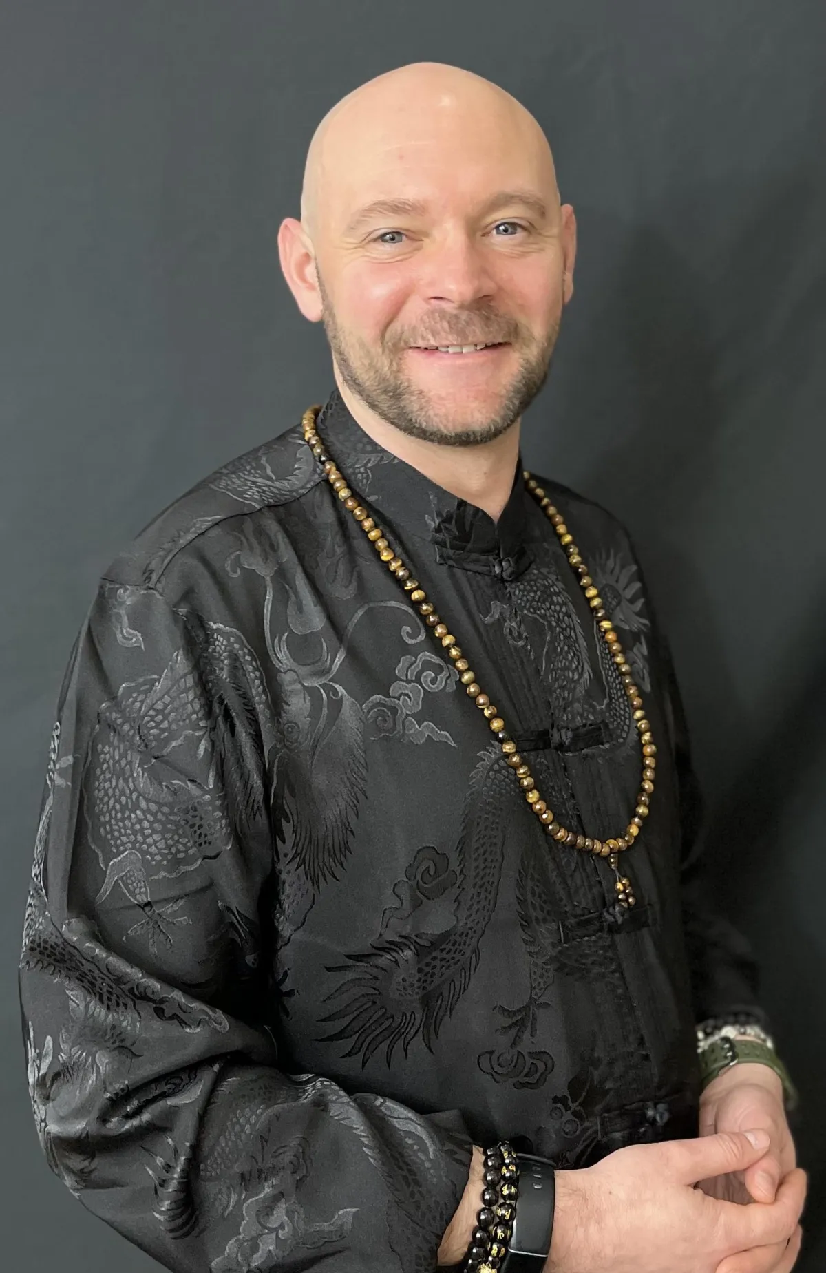 Baz Porter, transformational leadership coach and founder of RAMS by Baz™, photographed in a black dragon-patterned silk shirt with a gold-beaded necklace, exuding calm authority, authenticity, and grounded confidence.