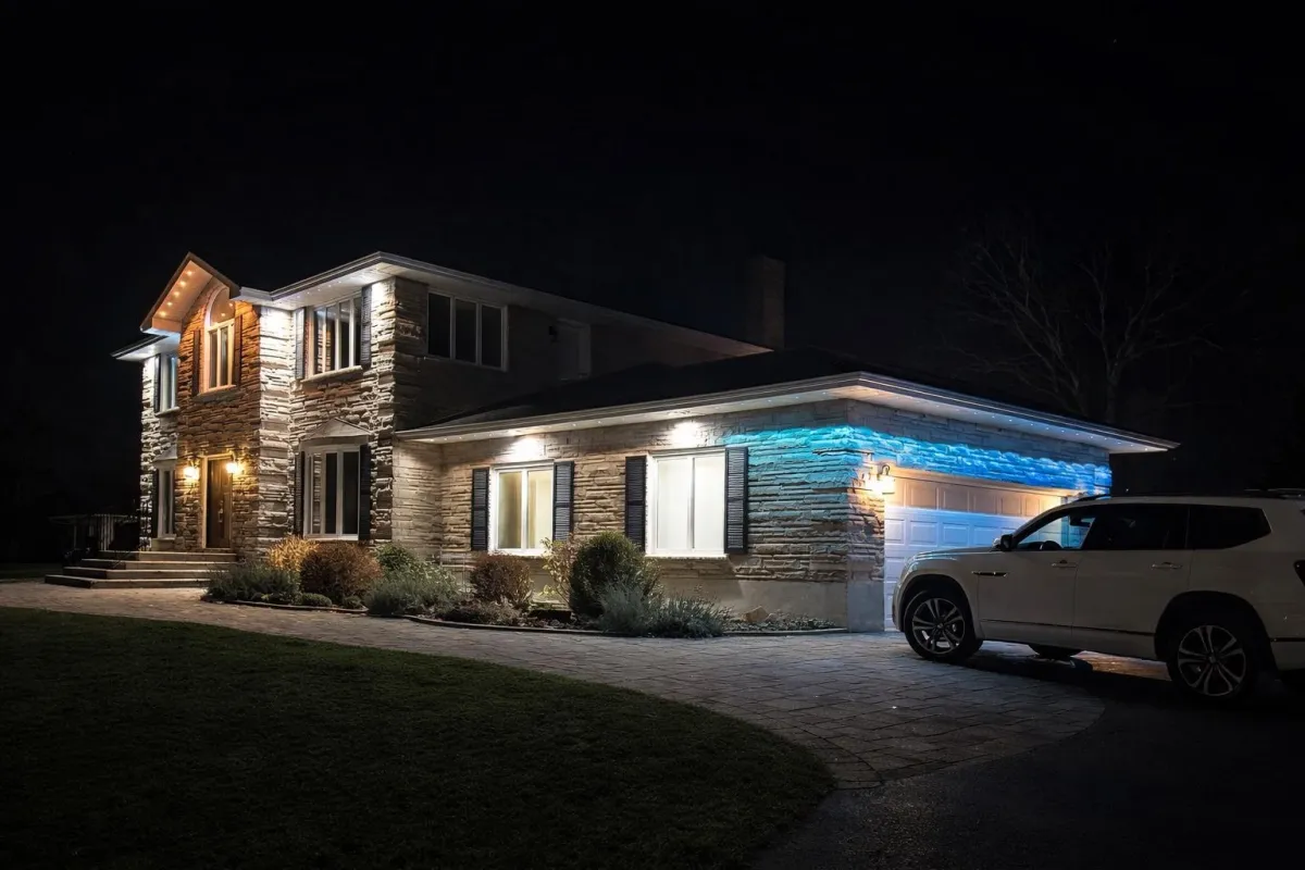 Stone home at night with white roofline lighting and a blue accent above the garage