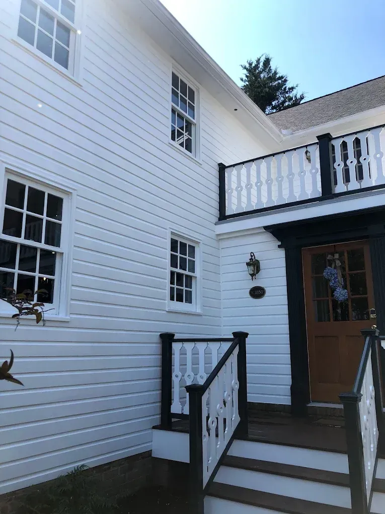 White residential house exterior with black trim, featuring decorative railing, windows, and a welcoming front door, showcasing Victory Painting's high-quality exterior painting services in Easton, MD.