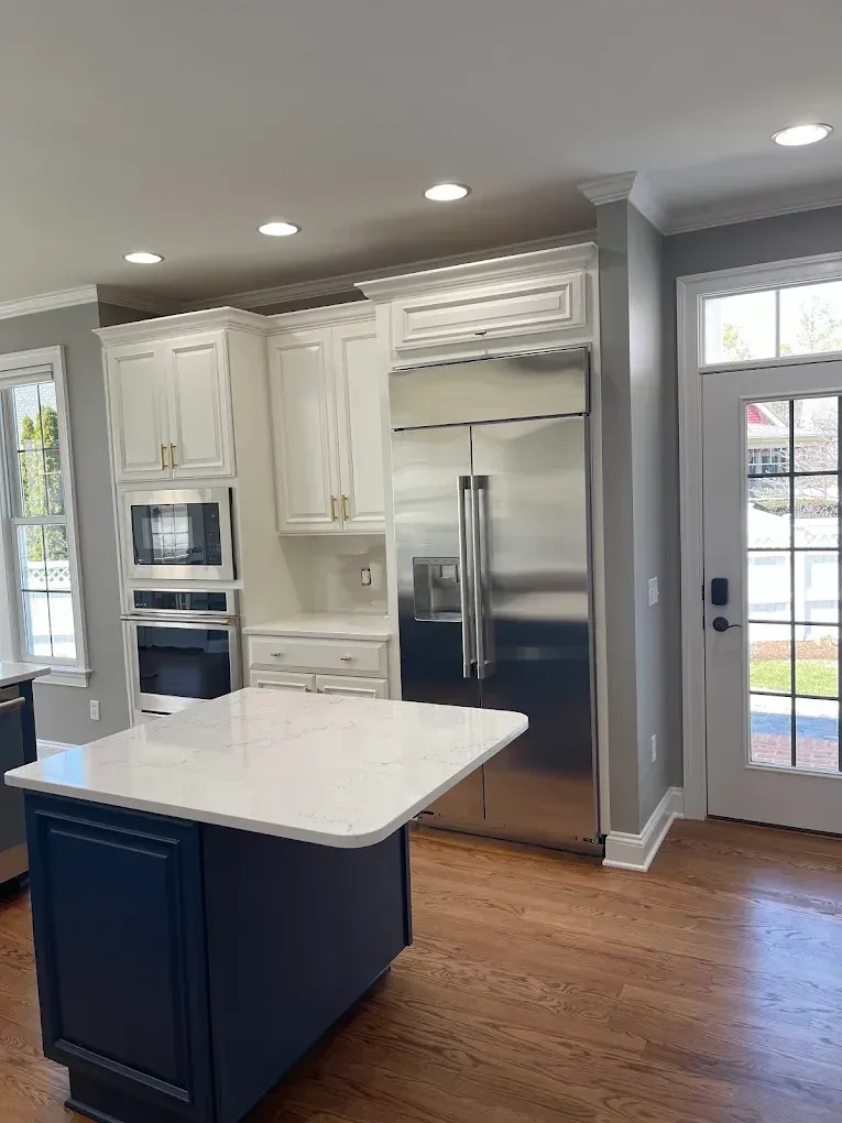 Modern kitchen interior featuring white cabinetry, stainless steel appliances, and a central island with a marble countertop, highlighting professional cabinet painting and refinishing services by Victory Painting LLC.