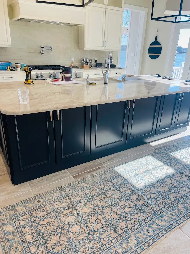 Modern kitchen with black cabinetry, marble countertop, and decorative rug, highlighting cabinet painting and refinishing services.