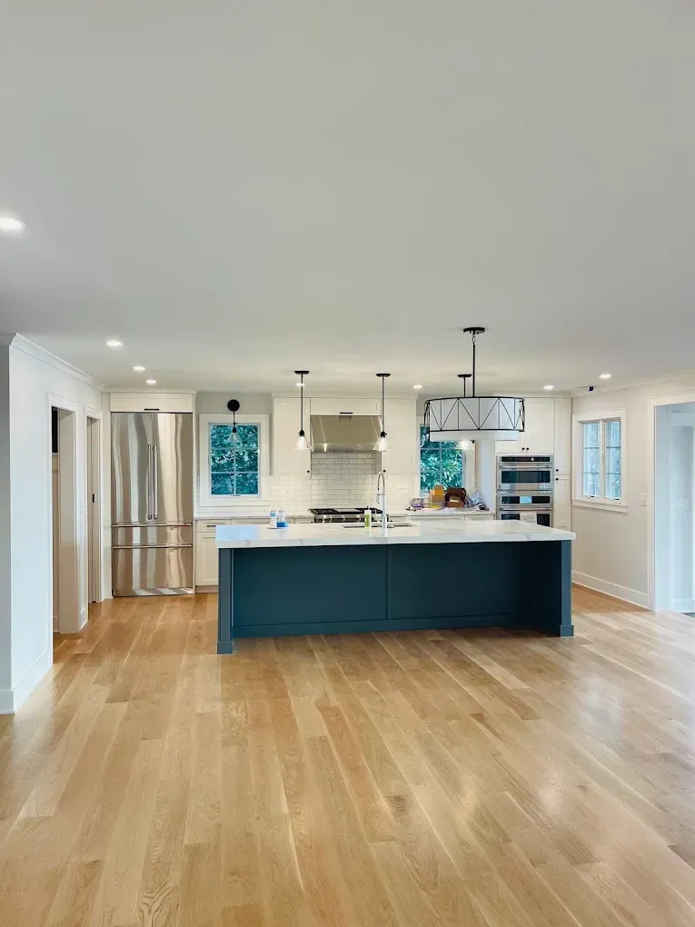 Modern kitchen interior featuring a spacious island with a dark blue base, stainless steel appliances, and bright, natural lighting, highlighting the potential for cabinet painting and refinishing services.