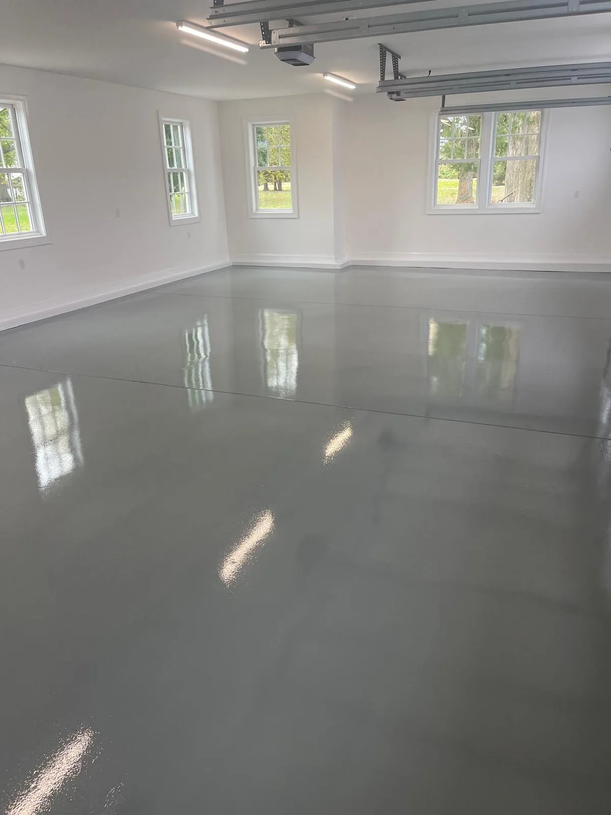 Seamless, glossy epoxy floor coating in a well-lit garage space with white walls and windows, showcasing professional finishing by Victory Painting LLC.