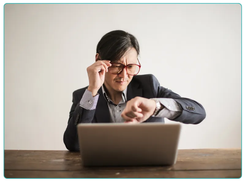 A woman in a suit and glasses intently examines her laptop screen.