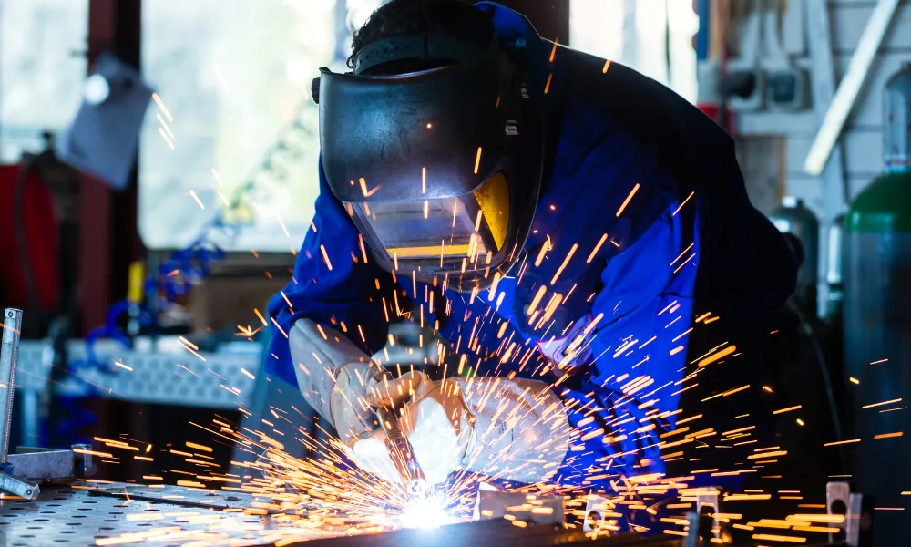 Welder in a workshop working on metal with sparks.