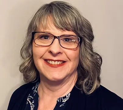 Woman with glasses smiling against a neutral background.