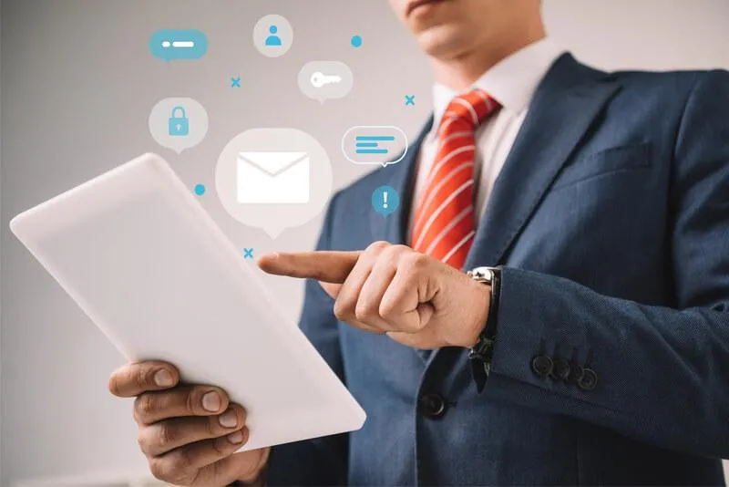 "Man in a suit tapping on a tablet displaying images of messages and icons, focused on technology and communication."