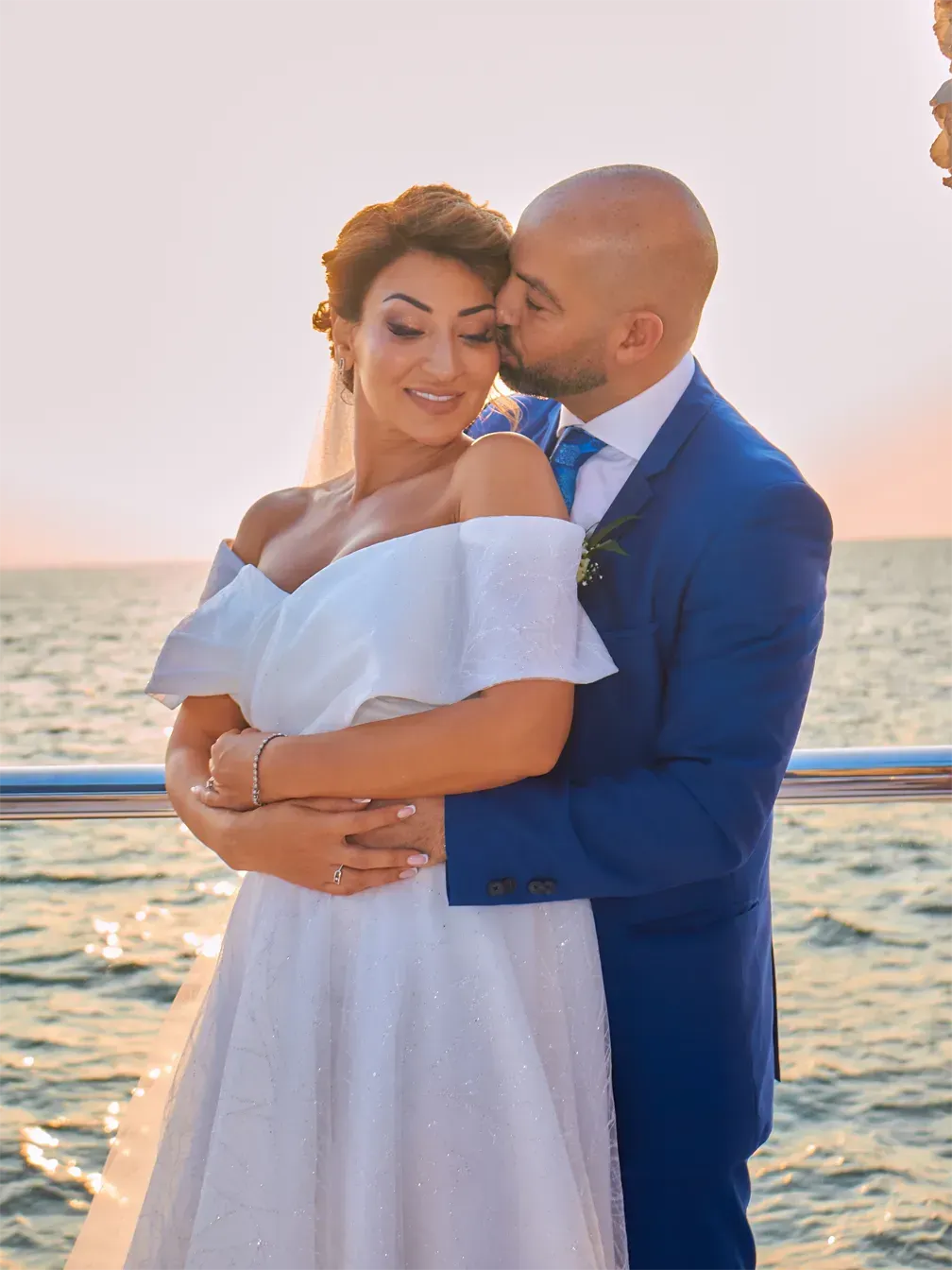 Ramy and Fatima on a rooftop at sunset during their wedding, Ramy in a navy suit, Fatima in a white dress.