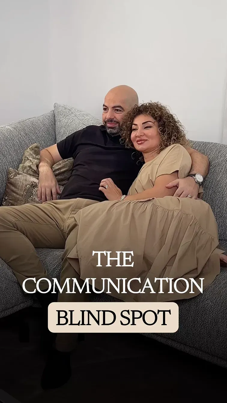 Ramy and Fatima sitting closely together on a grey sofa, relaxed and smiling at the camera, dressed in matching earth tones.