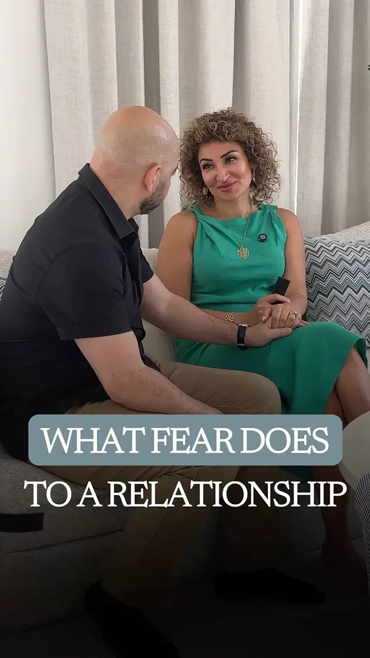 Ramy leaning in attentively toward Fatima, who sits across from him on a sofa in a teal dress, holding his hand and smiling.