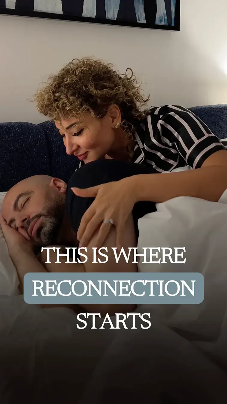 Fatima leaning over Ramy as he rests on a pillow, her hand on his chest, both relaxed and sharing a tender moment.