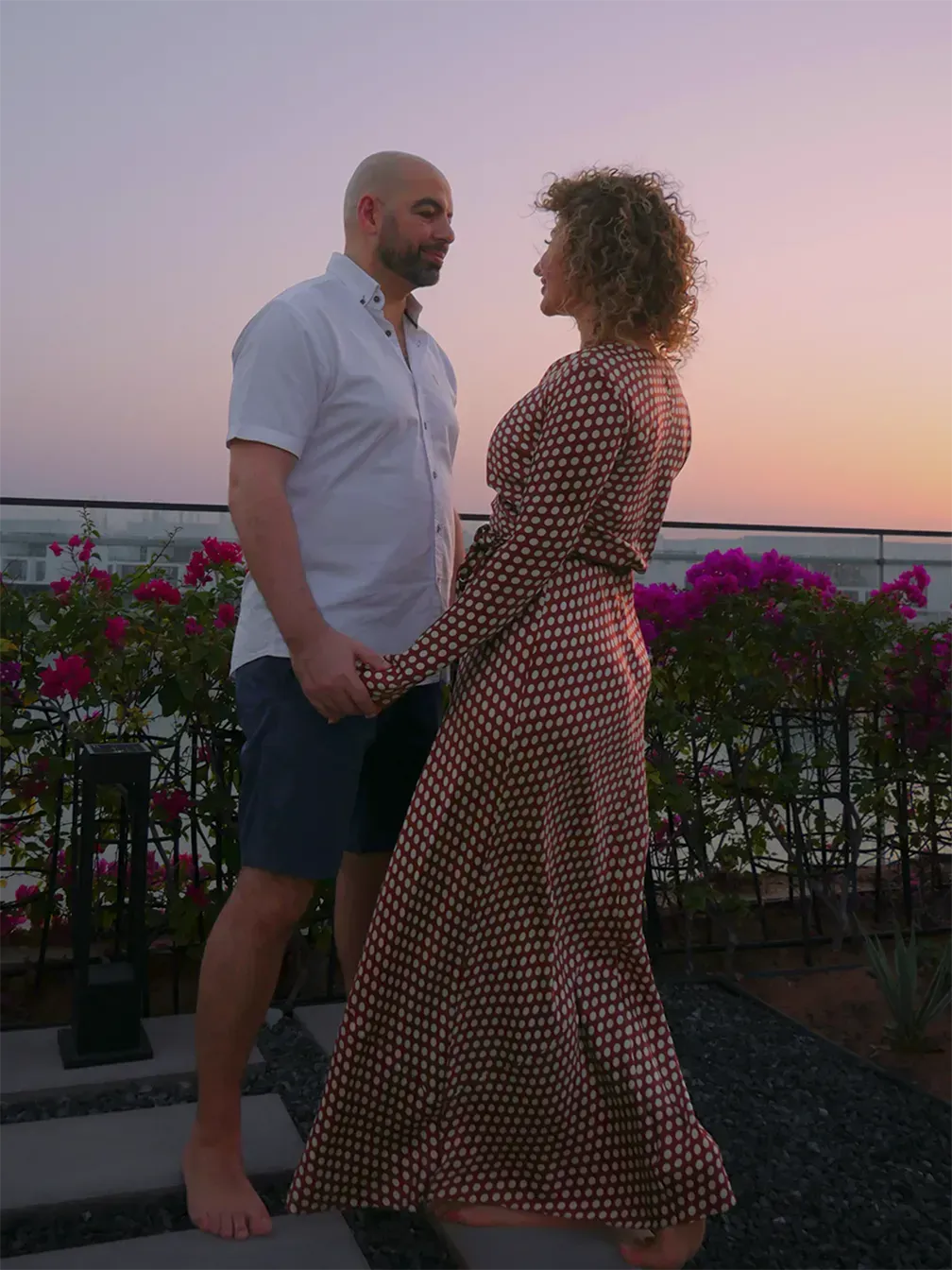 Ramy and Fatima standing face to face outdoors at dusk, holding each other's gaze.