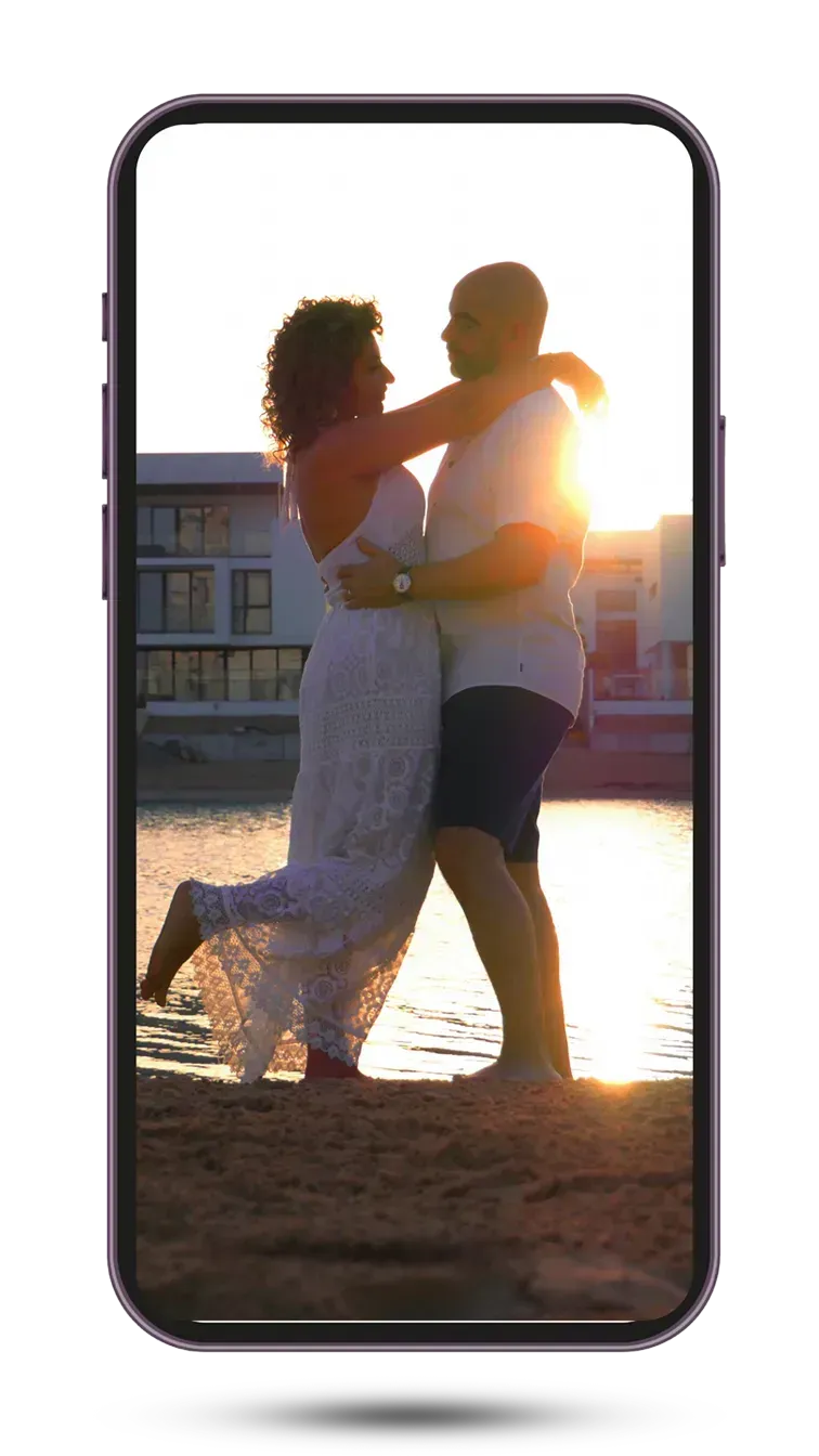 Ramy and Fatima embracing at sunset by the water, Fatima's arms around Ramy's neck.