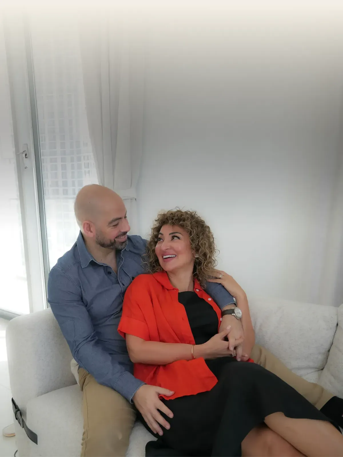 Ramy and Fatima laying on the couch and smiling at each other. 