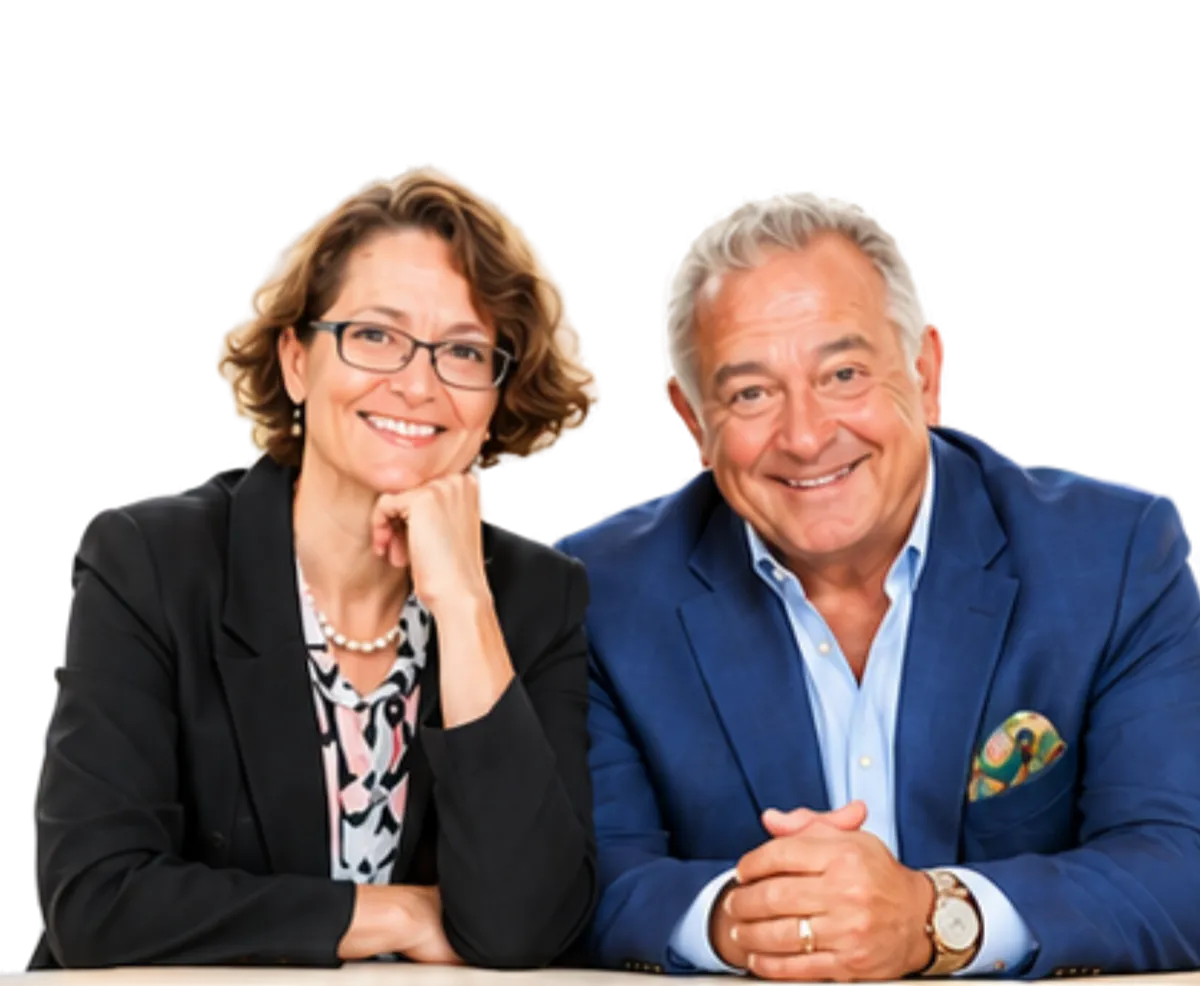 Older couple, a woman and a man, smiling warmly at the camera. The woman wears glasses and a black blazer. The man wears a blue blazer.