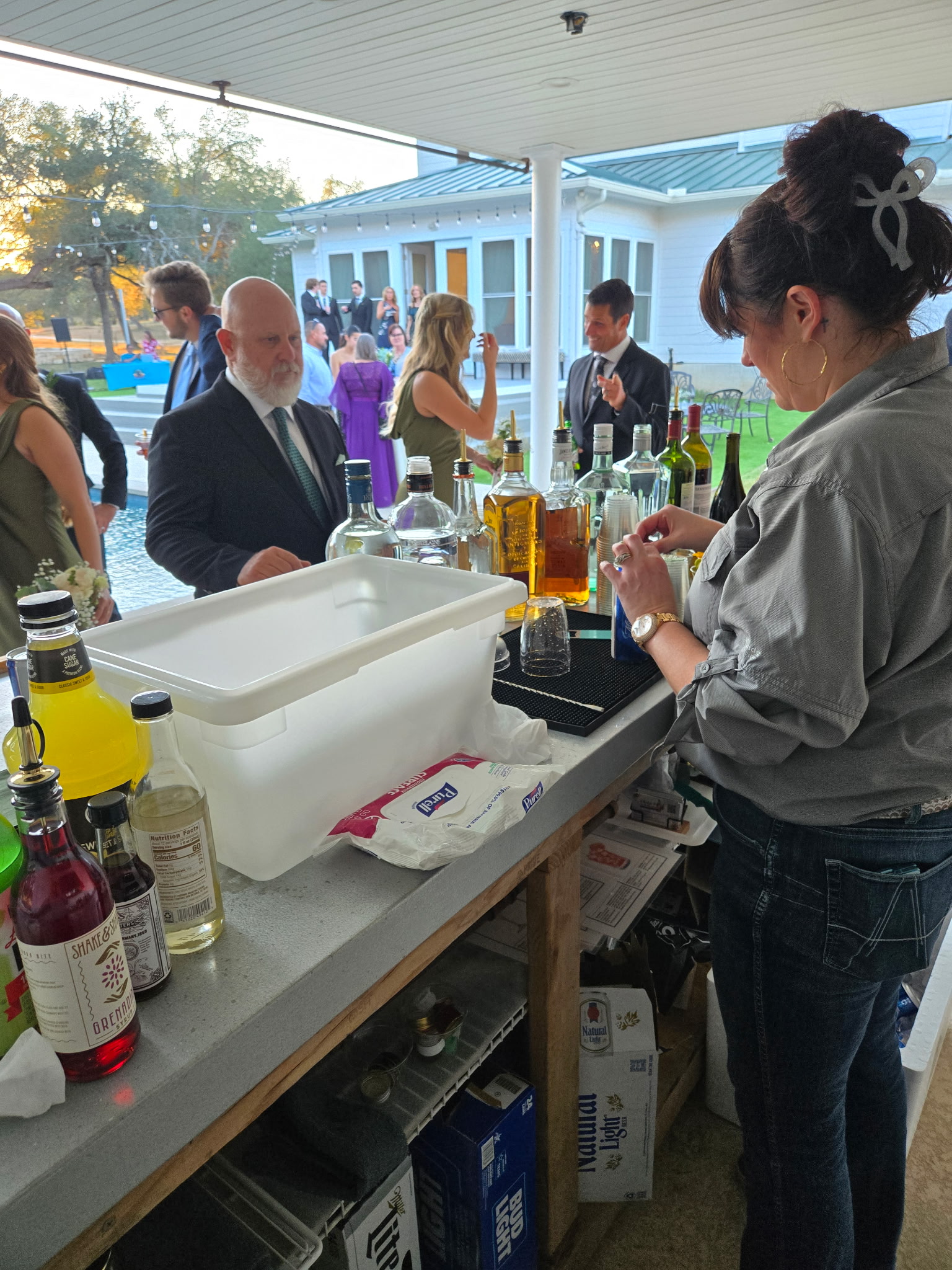 Bartender serving drinks from a stocked bar table at an outdoor Texas wedding reception