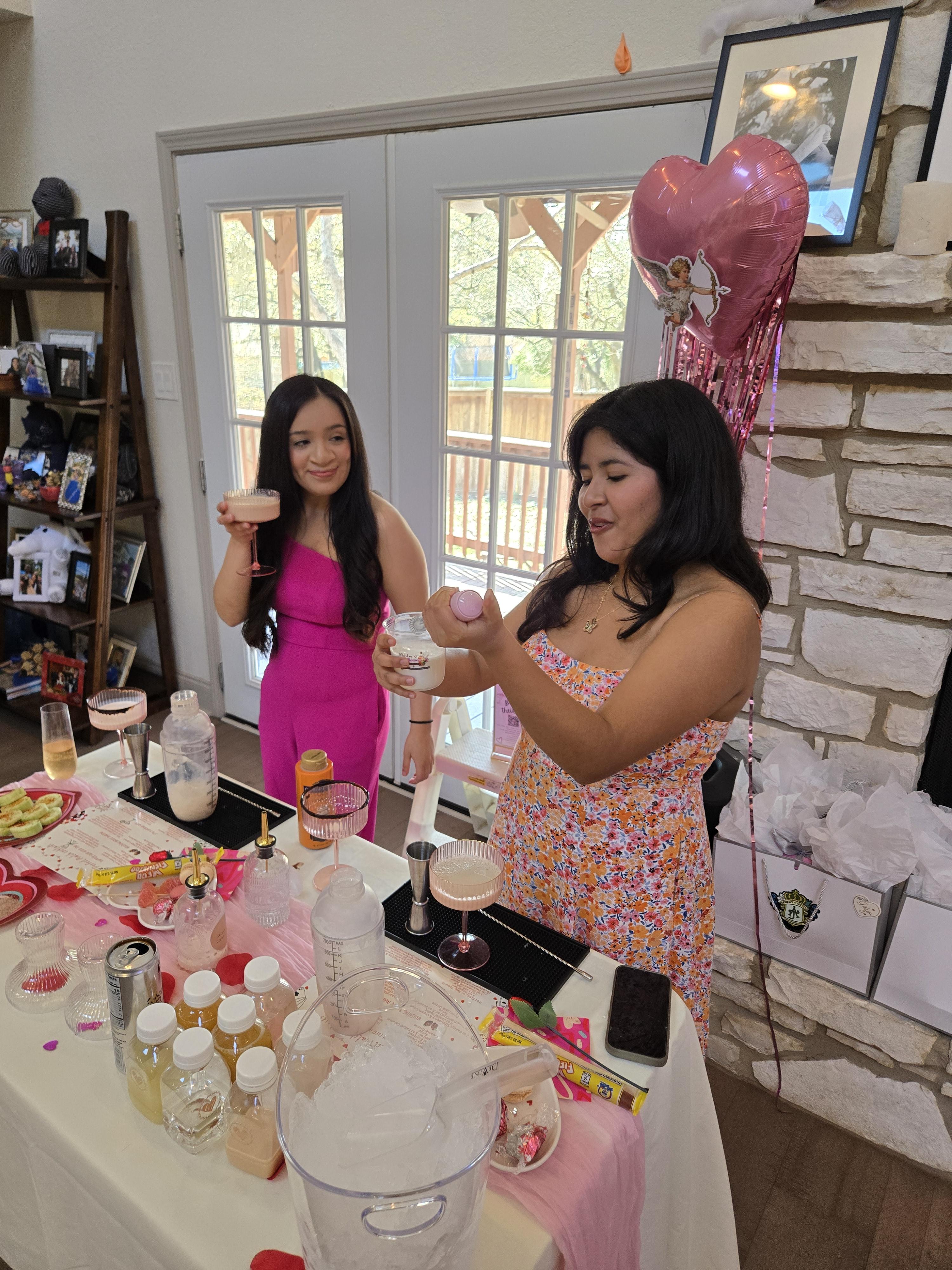 Two guests in pink dresses mixing cocktails together at an indoor mixology party celebration