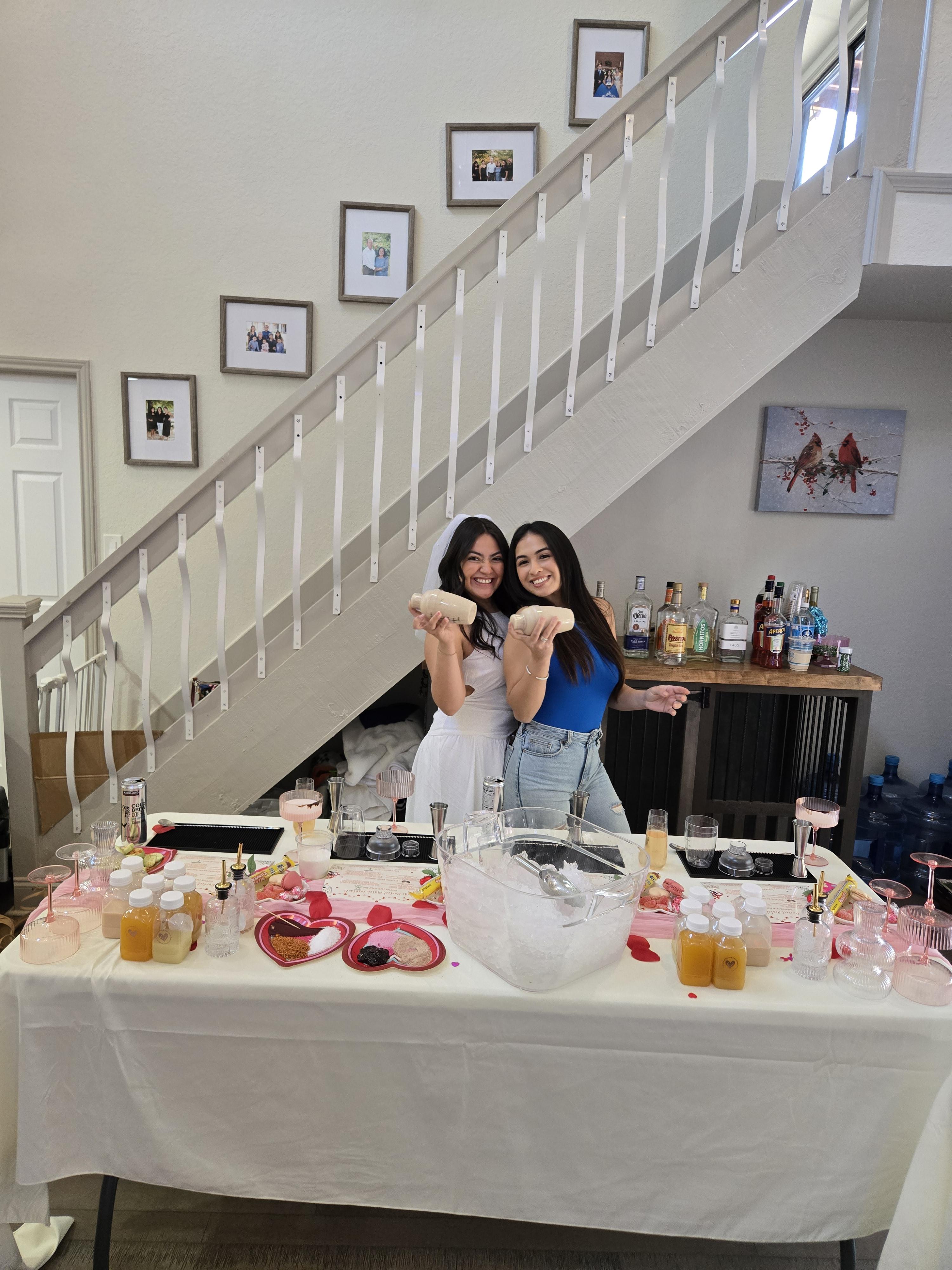 Two guests smiling and shaking cocktail shakers at an indoor bachelorette mixology party