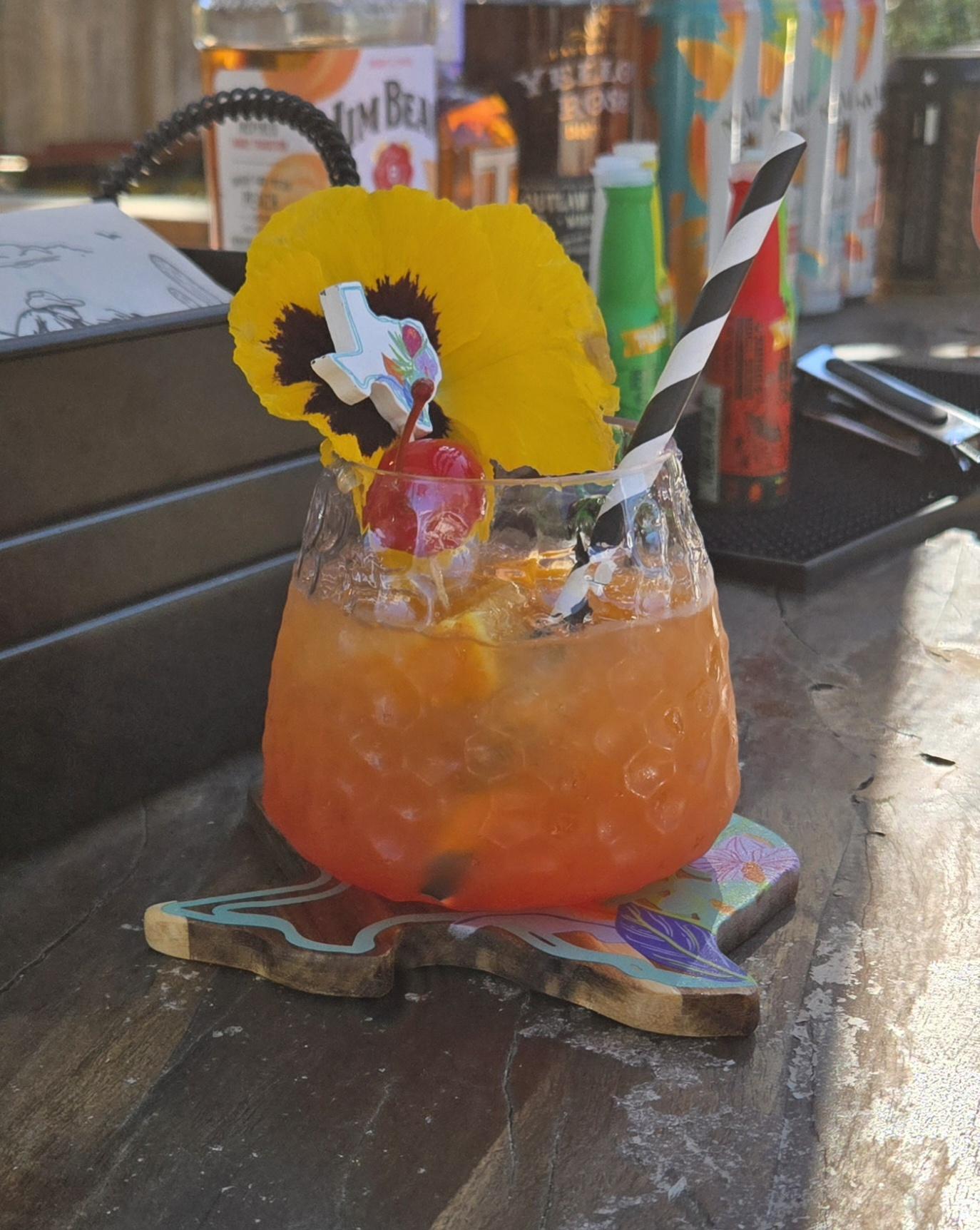 Orange citrus cocktail garnished with a dried flower and striped straw