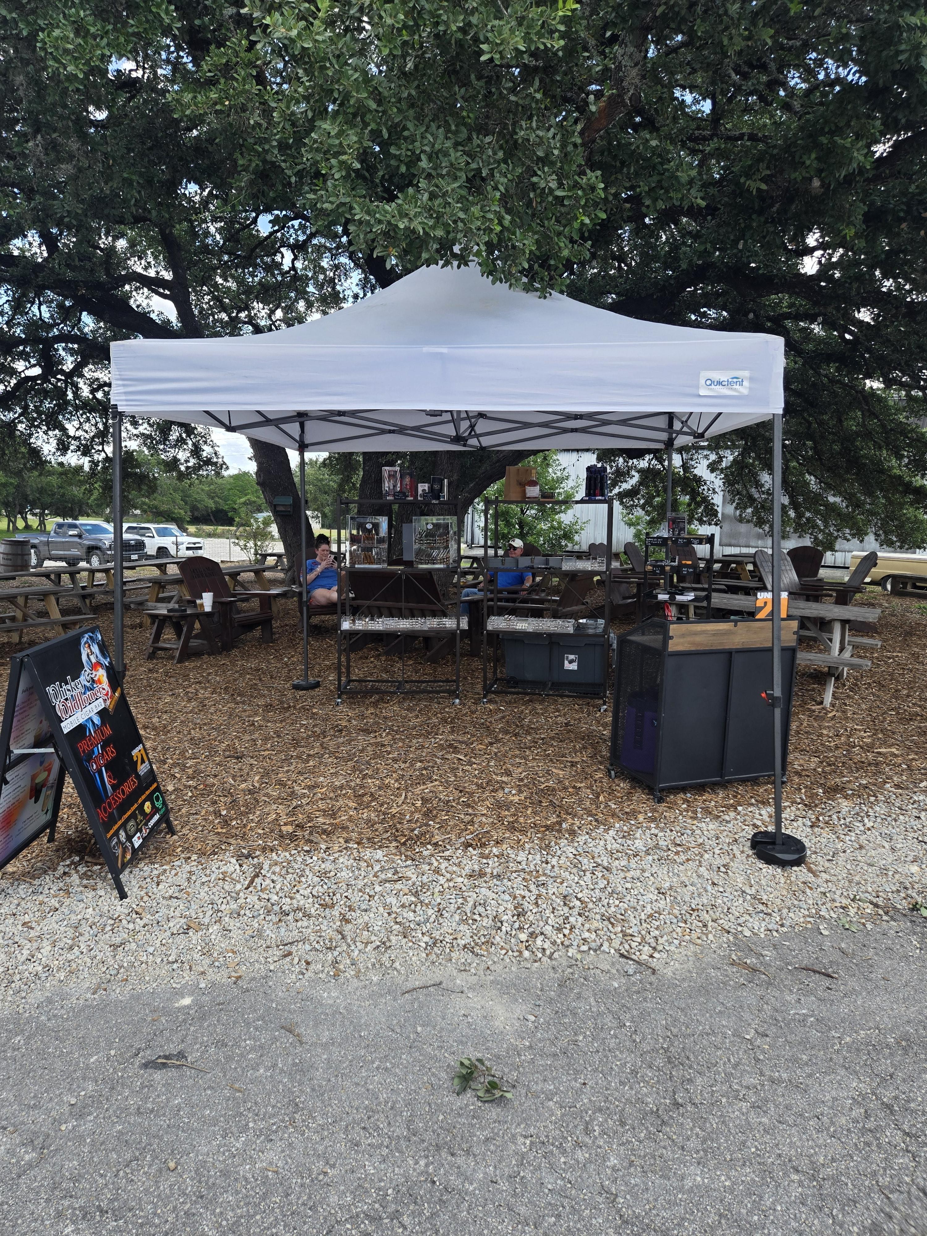 Whiskey and Wildflowers cigar bar tent setup under oak trees at an outdoor pop-up