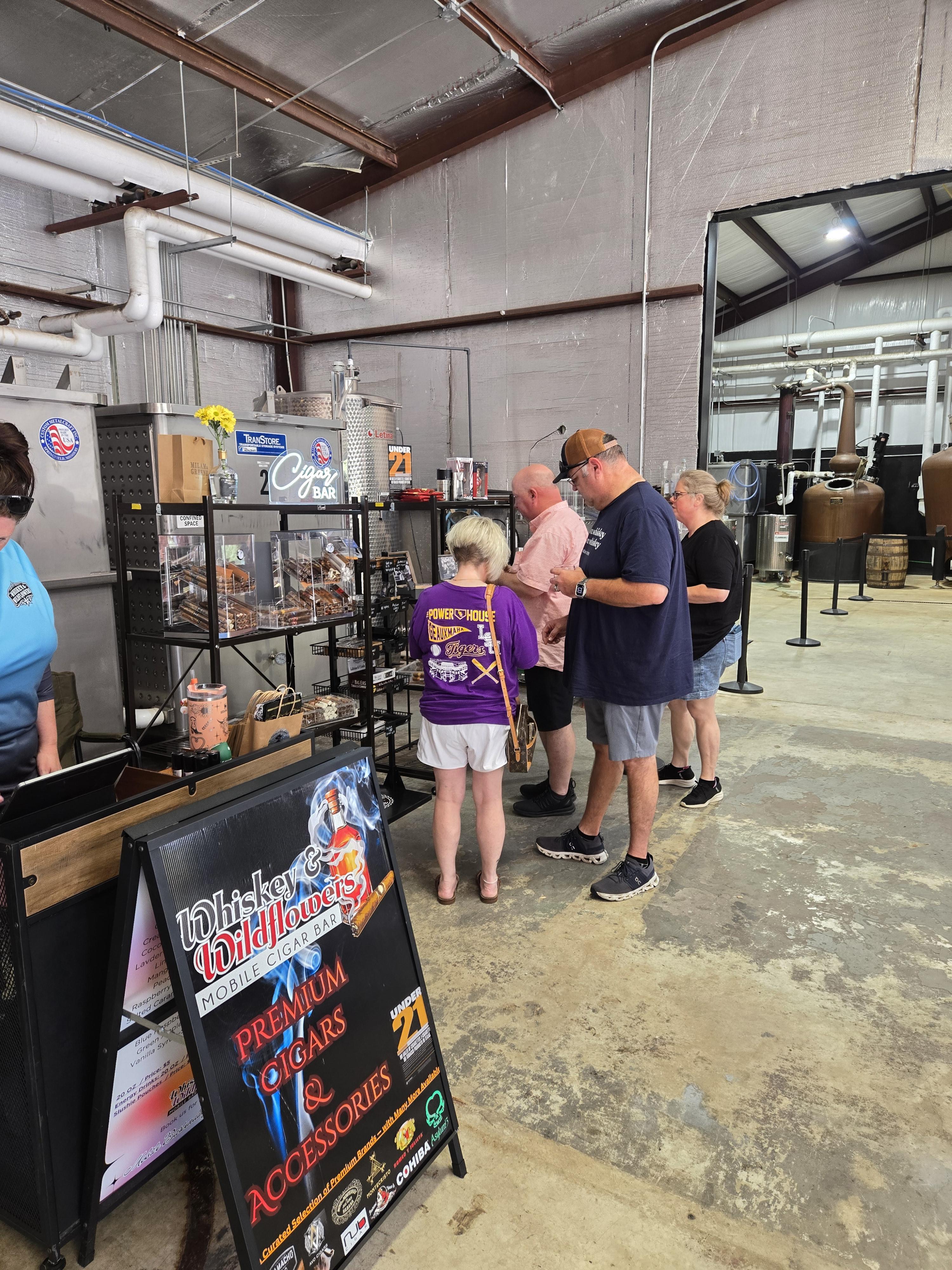 Guests browsing the Whiskey and Wildflowers cigar case at an indoor distillery pop-up