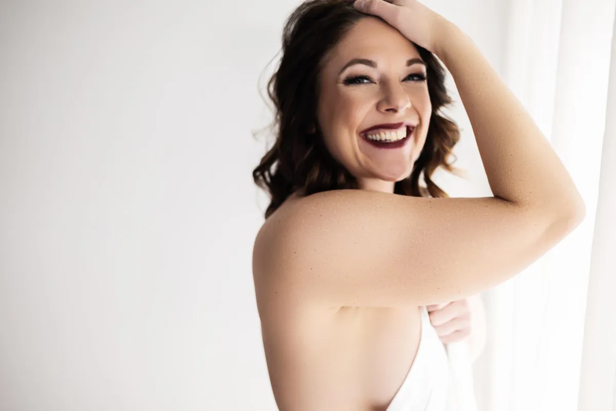 Minneapolis Boudoir woman smiling with bed sheet covering her