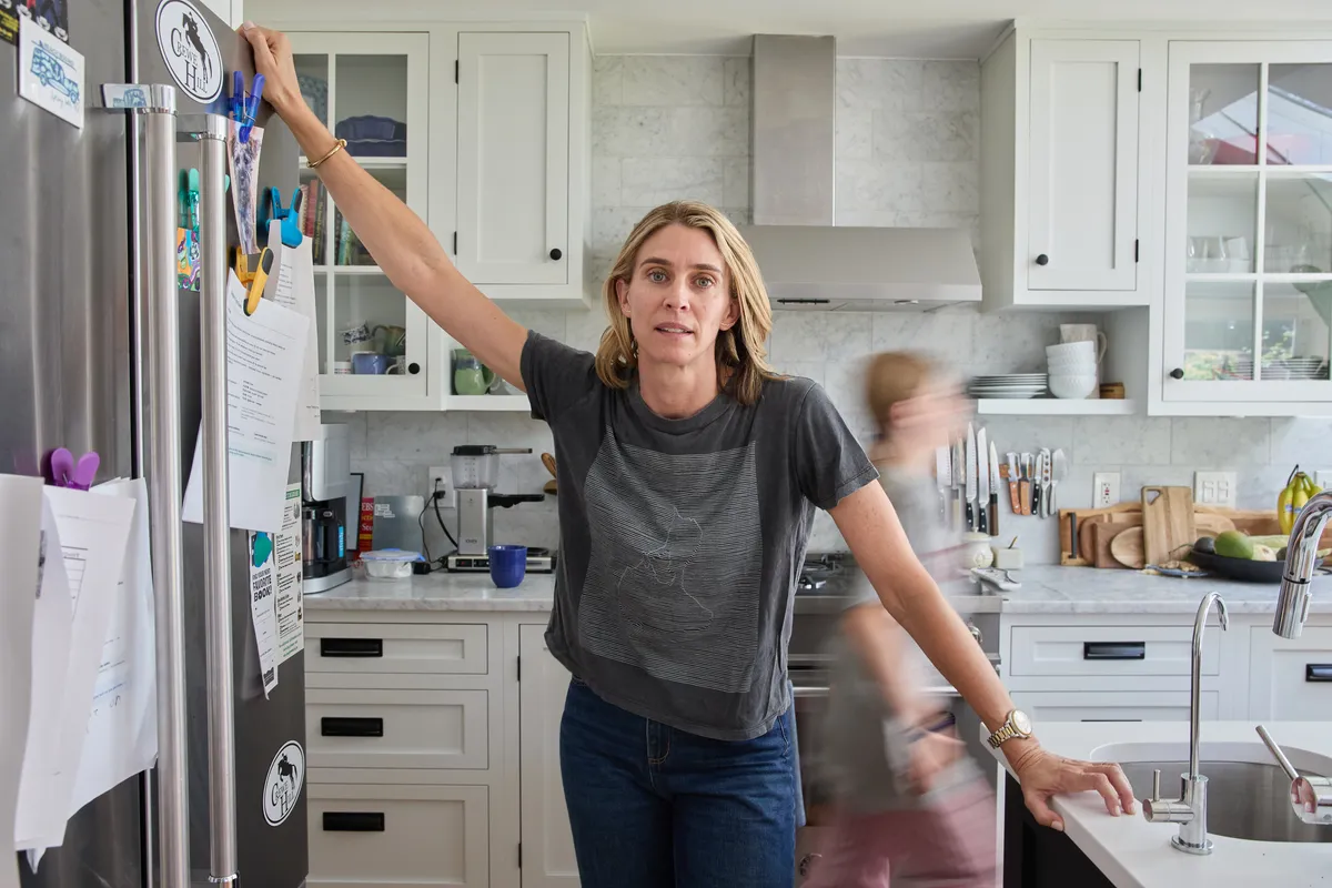 Maris Pasquale Doran bracing between the fridge and the sink, looking at the camera, her son blurred in motion behind her.