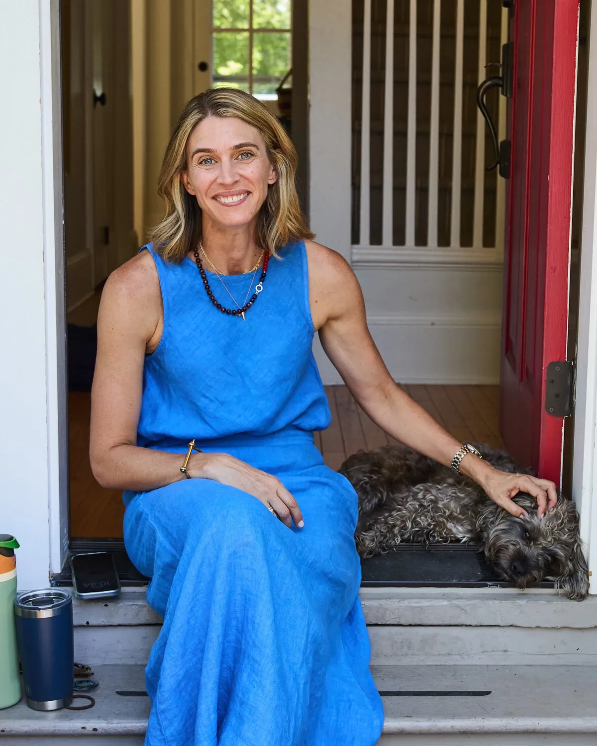 Maris Pasquale Doran seated in her red front doorway with her dog Wylie