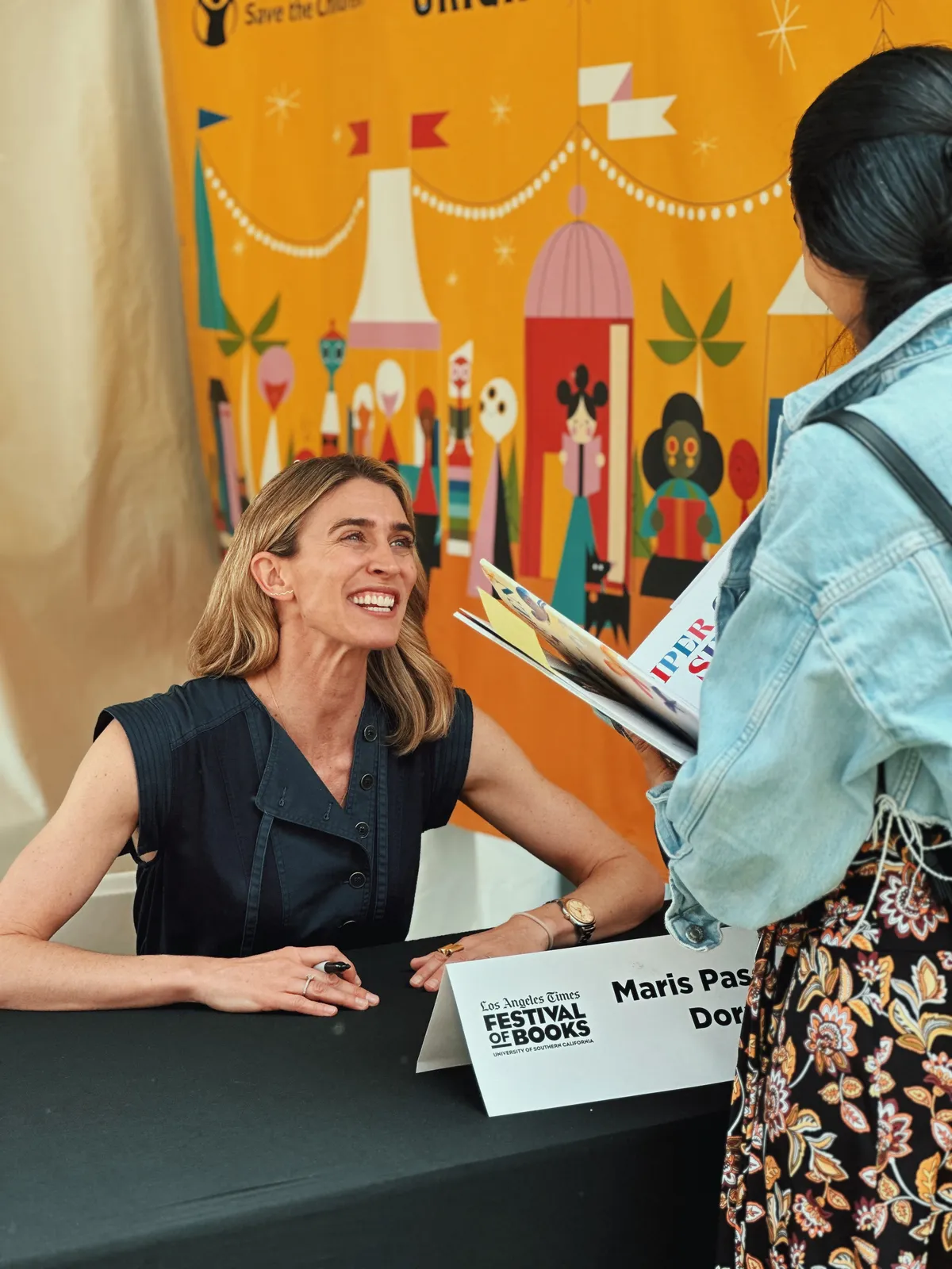 Maris Pasquale Doran at LATimes FOB book signing table, a young reader leaning in.
