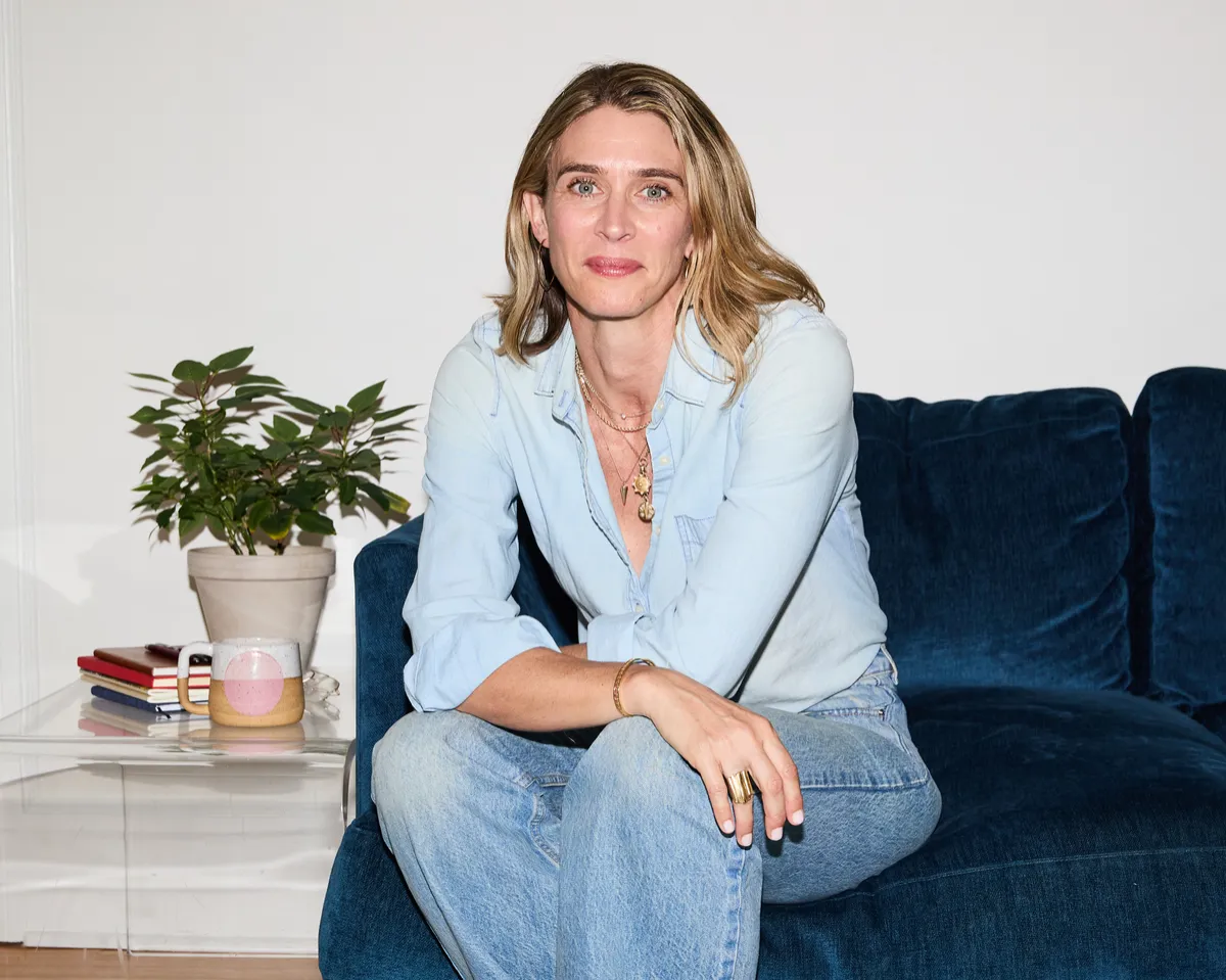 Maris Pasquale Doran leaning forward on a couch, hands over knees, with a slight smile.