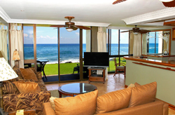 A modern, open-concept kitchen with stainless steel appliances, white quartz countertops, and a breakfast bar. Sunlight streams in from a large window, highlighting fresh tropical fruit on the counter.