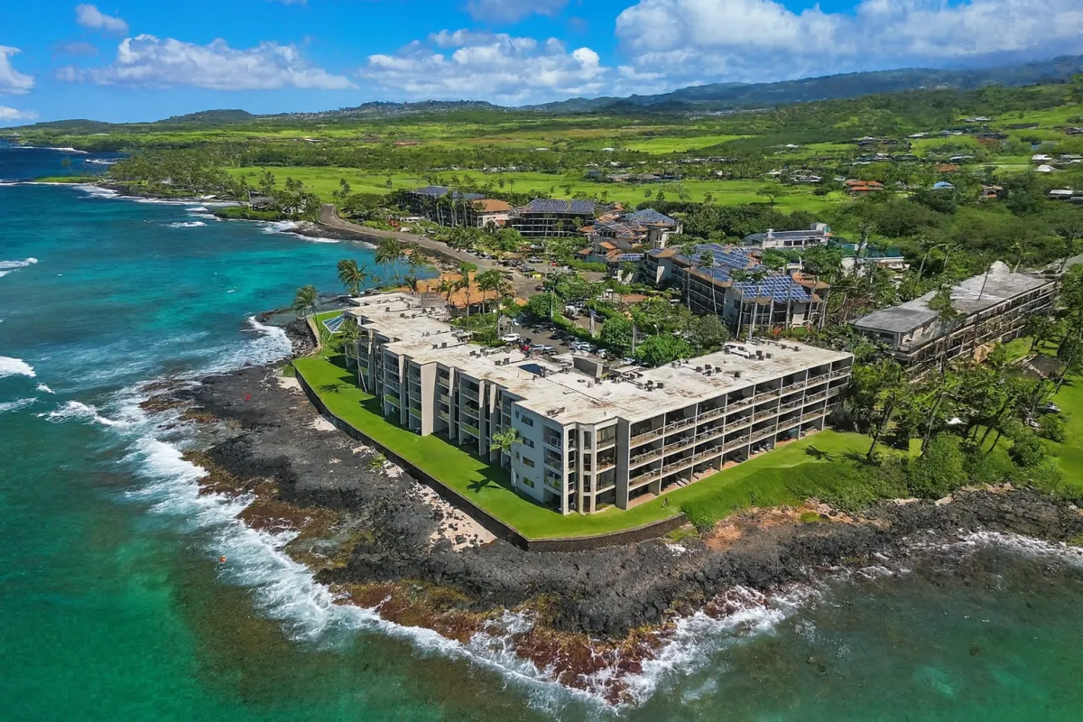 A sunlit, modern living room with floor-to-ceiling windows opening to a sandy beach and turquoise ocean, tropical plants outside, and a cozy seating area inside. The scene is bright, airy, and inviting, perfect for a relaxing vacation.